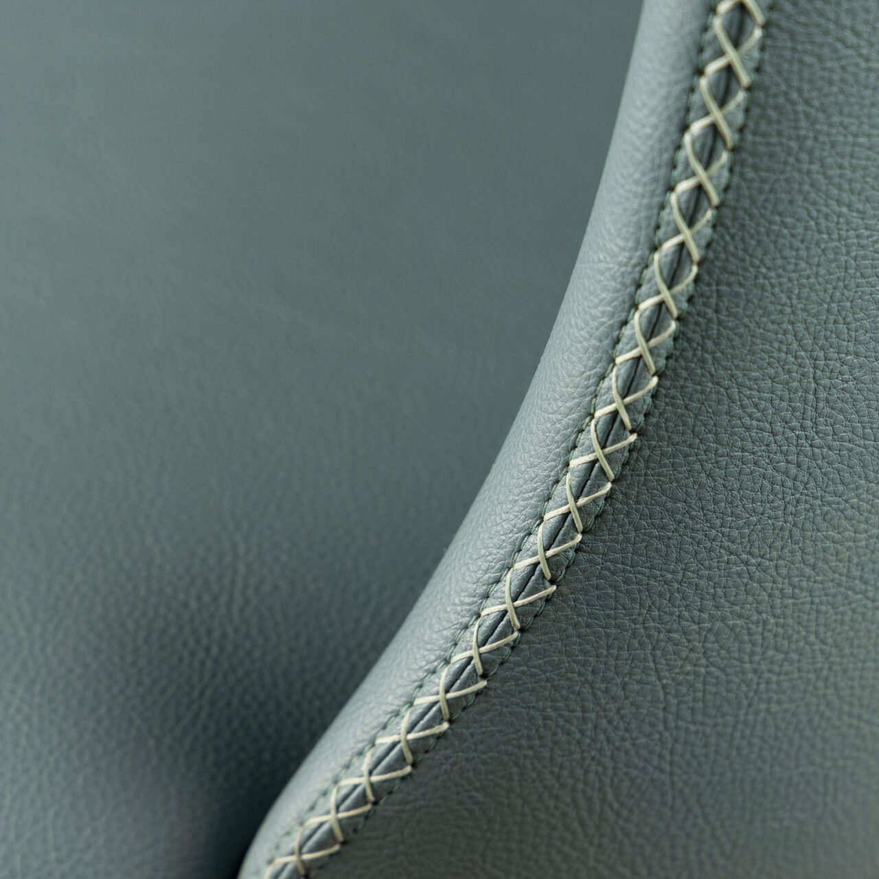 A close-up of SENTIENT Furniture's custom upholstery detailing, highlighting the meticulous gray leather stitching along the edge of a high-quality, handcrafted seat.