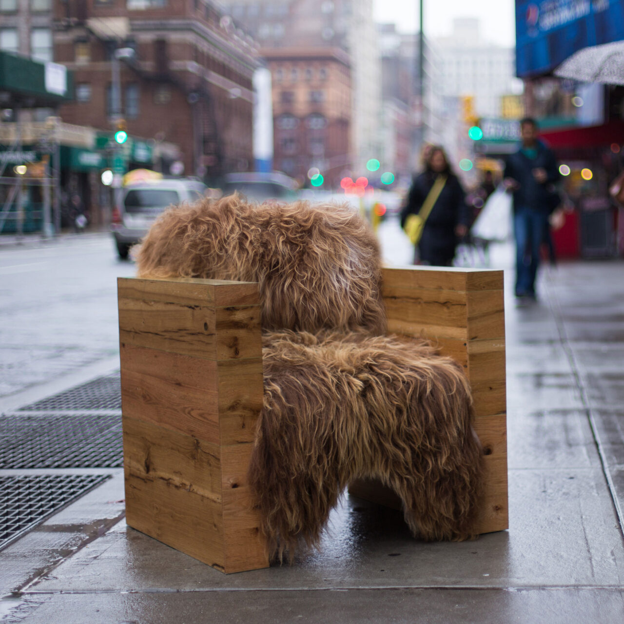 SENTIENT's Joojay luxury armchair placed outdoors, crafted from textured wood and covered with a thick, shaggy brown sheepskin, blending with the urban surroundings.