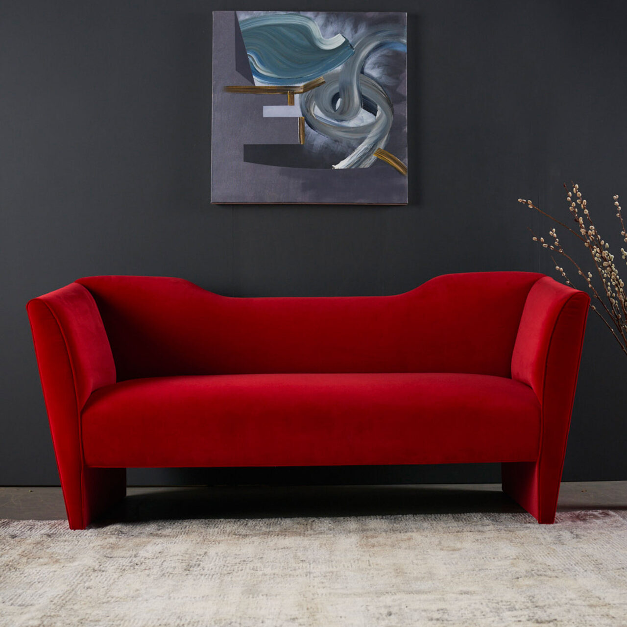 A SENTIENT Nersi sofa in rich red fabric, showcasing a modern silhouette with flowing lines, complemented by abstract art and a rustic rug.