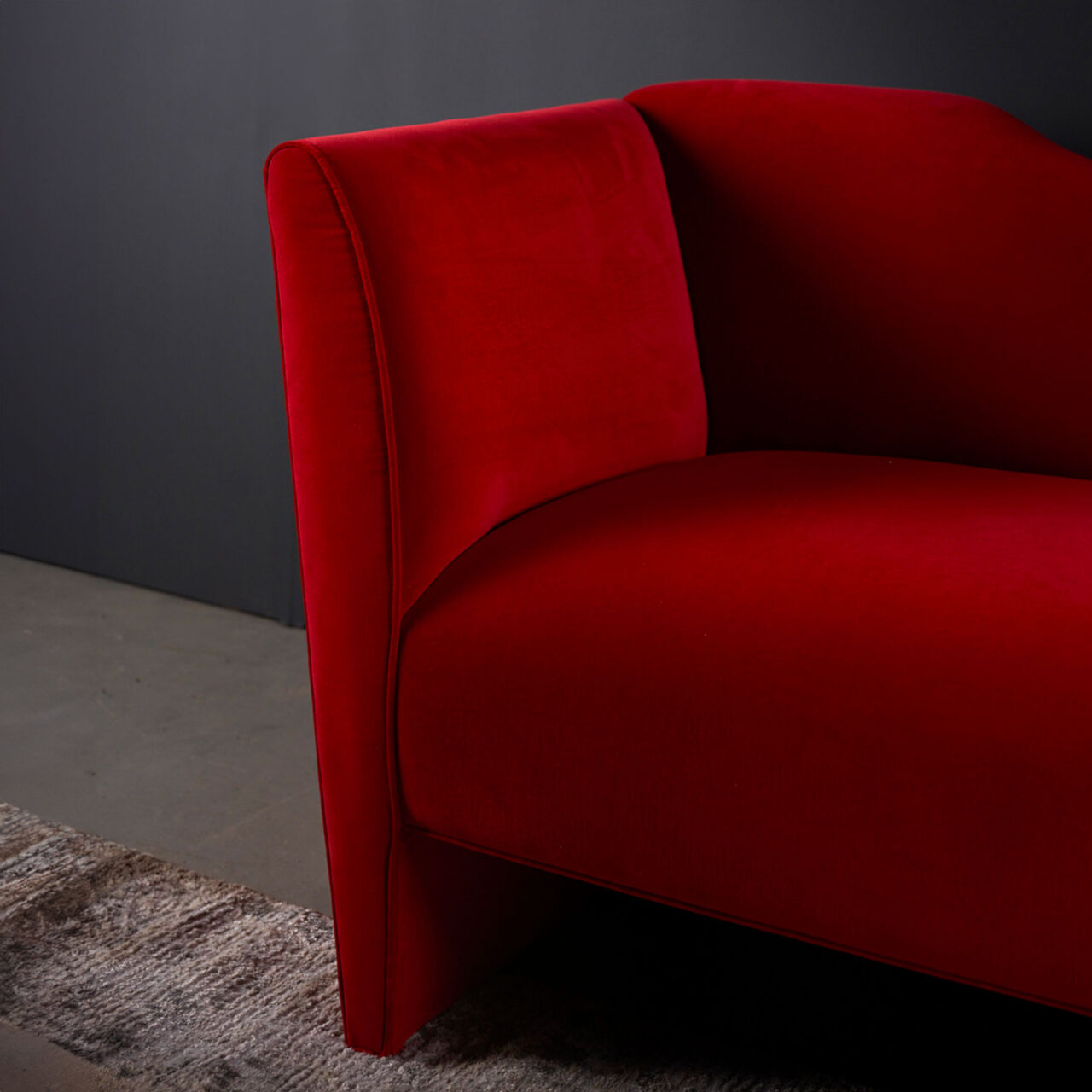A bold and luxury SENTIENT Nersi sofa in vibrant red upholstery, with a curved backrest and a plush, inviting seat, in a room with a dark gray wall.