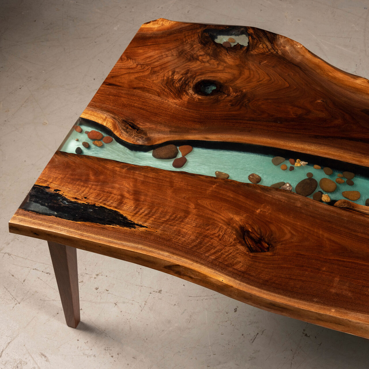 SENTIENT's epoxy river table is a masterpiece of craftsmanship, where the swirling patterns of natural wood are juxtaposed with a stream of translucent blue resin.