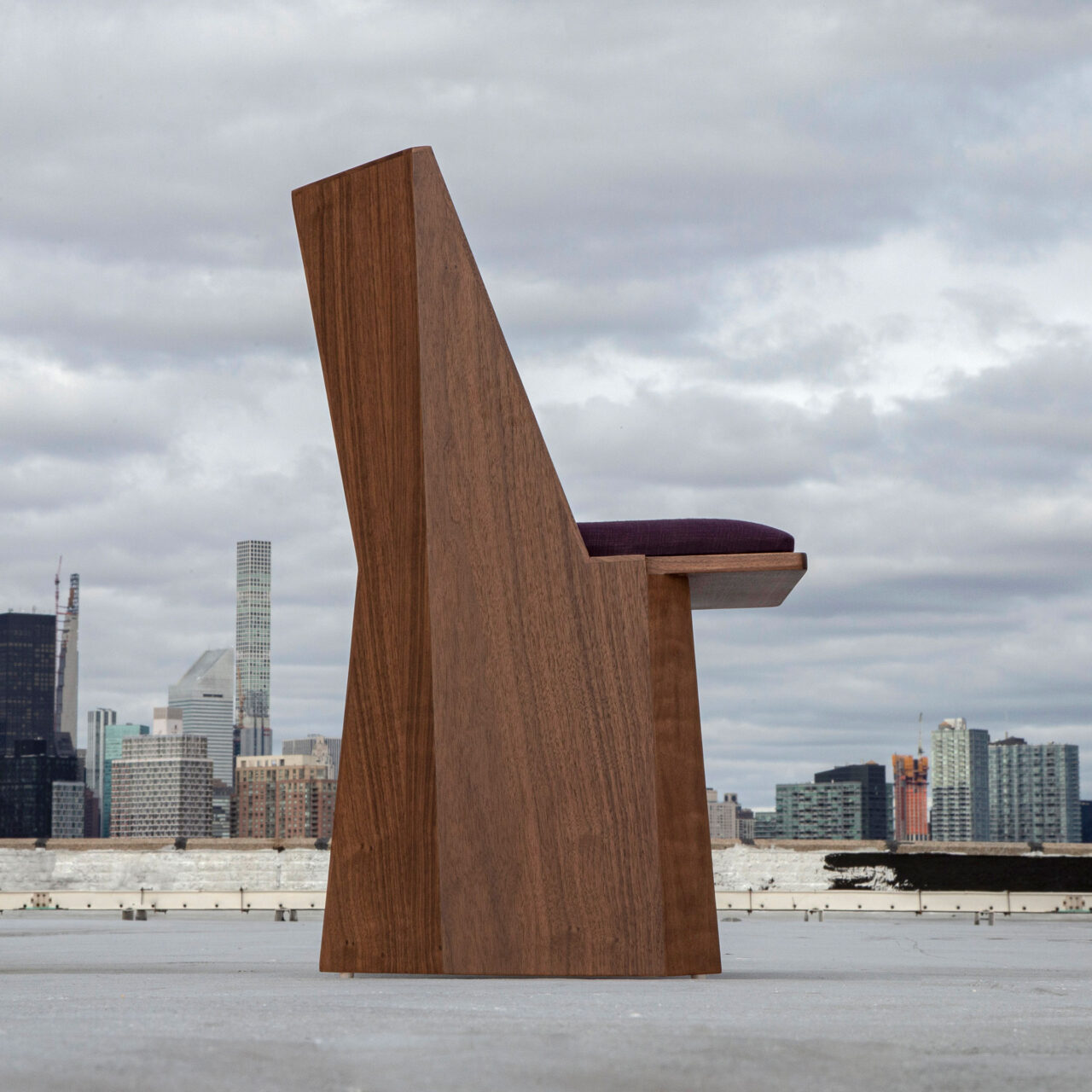 Striking model of unique dining chairs, the 'Symphony Chair' by SENTIENT Furniture, an innovative wooden chair with a tall, angular backrest and a deep purple cushion, overlooking a city skyline.