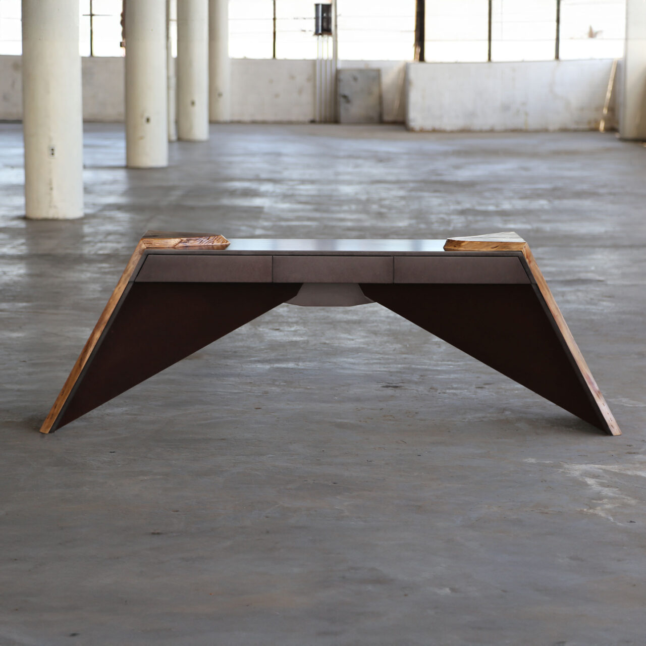 The 'Time When Console' by SENTIENT Furniture, a unique walnut table with angular legs and natural edge details, displayed in a spacious industrial setting.